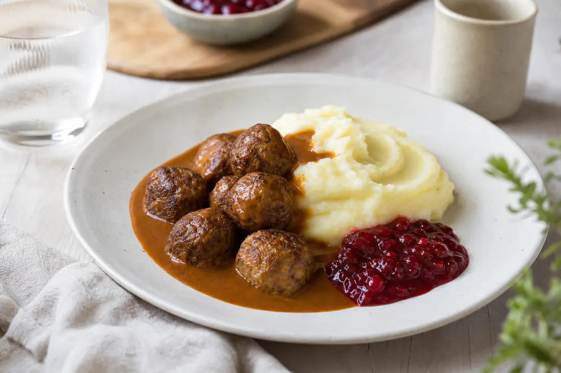 Ruskistuneet lihapullat lautasella perunamuusin, ruskean kastikkeen ja puolukkahillon kanssa