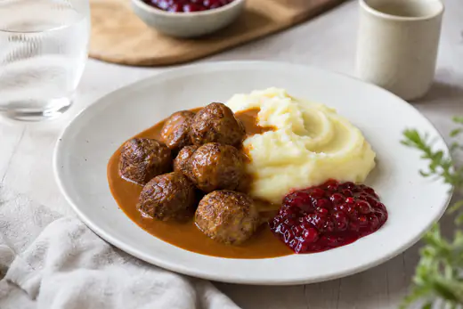 Ruskistuneet lihapullat lautasella perunamuusin, ruskean kastikkeen ja puolukkahillon kanssa