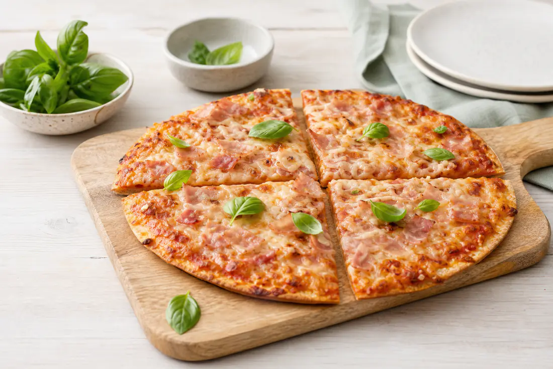 Neljään osaan leikattu paistettu pakastepizza kinkulla ja sulaneella juustolla leikkuulaudalla