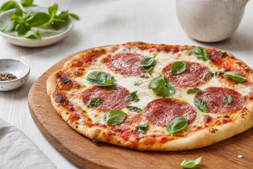 Pieni kotitekoinen salamipizza sulaneella mozzarellalla ja basilikalla puisella tarjoilulaudalla